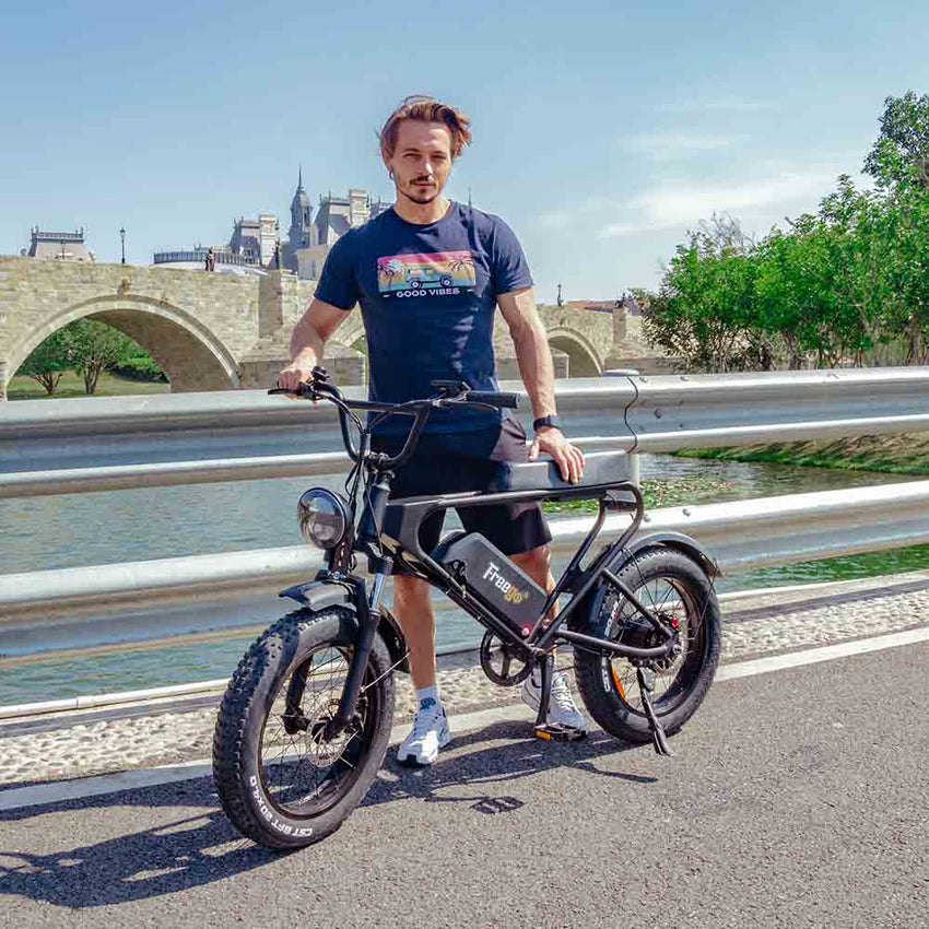 Freego DK200 fat tire e-bike with rider beside a river and stone bridge