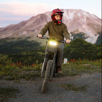 Freego Nova 4 electric dirt bike with headlight on, rider below a mountain