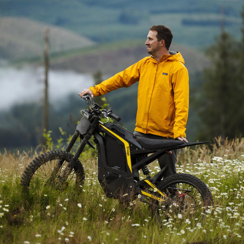 Freego Nova 4 electric dirt bike parked in a grassy field with rider standing beside
