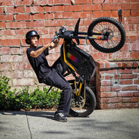 Freego Nova 4 electric dirt bike rider doing a wheelie beside a brick wall