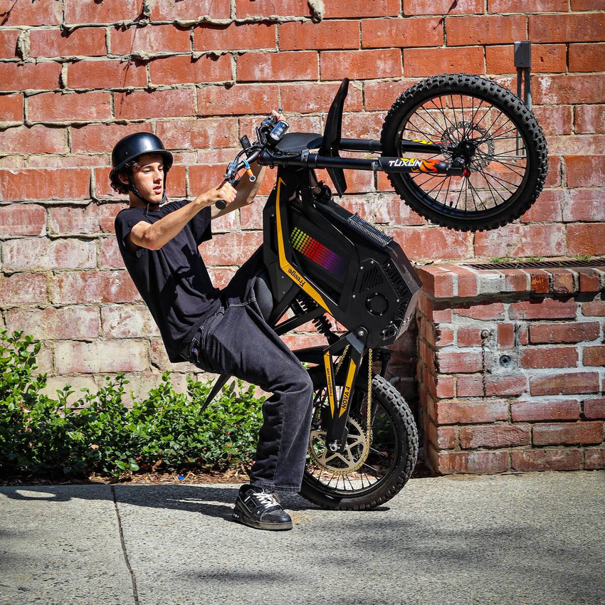 Freego Nova 4 electric dirt bike rider doing a wheelie beside a brick wall