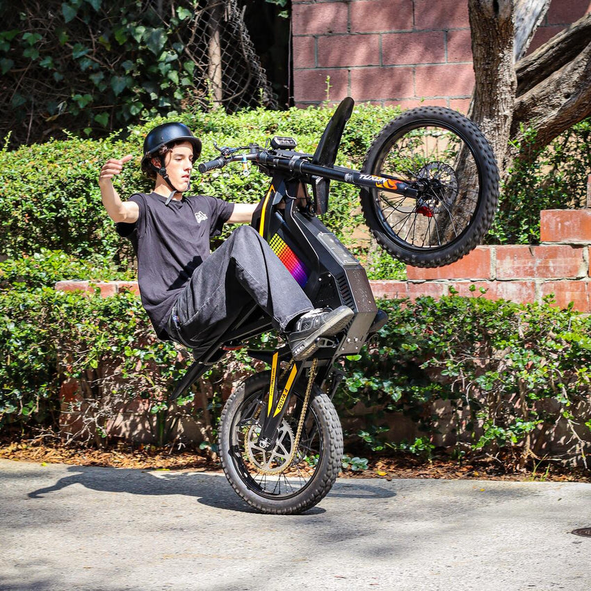 Freego Nova 4 electric dirt bike wheelie in a parking lot with hedges