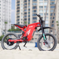 Freego X2 Pro Red Limited electric dirt bike on a sandy beach with high-rise buildings behind